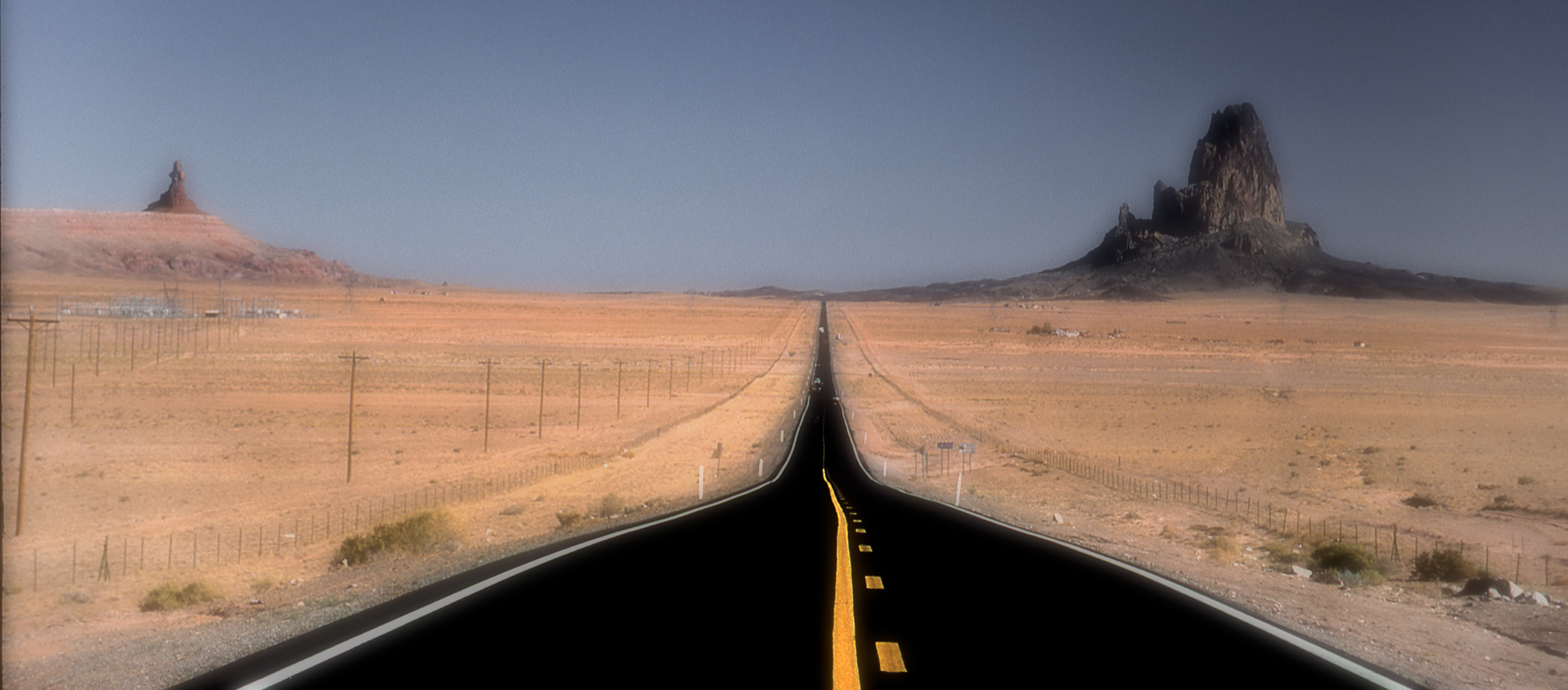 Photo d'une route noire avec des bandes jaunes menant au site de Monument Valley au usa avec des pics rocheux en arrière plan.